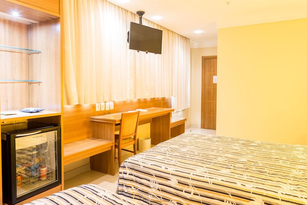 ריו דה ז'ניירו Hotel Atlantico Business Centro מראה חיצוני תמונה The photo shows a hotel room with two beds featuring striped bedding. There is a wooden desk and chair near a window with light-colored curtains. A flat-screen television is mounted on the wall, and there appears to be a small refrigerator or mini-ba